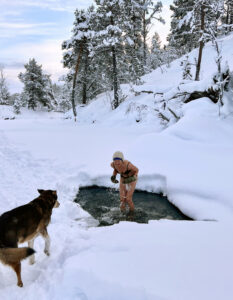 dame som bader i et hull i isen mens hunden passer på