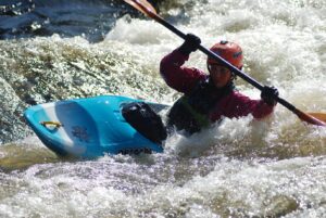 gutt i elvekajakk, blå kajakk og rød hjelm