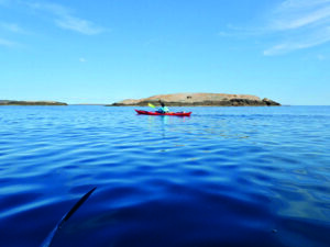 Mann i rød kajakk på blått hav og øy i bakgrunnen