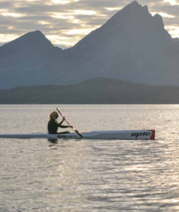 padlende kvinne med surfski og en siluett av høye fjell bak